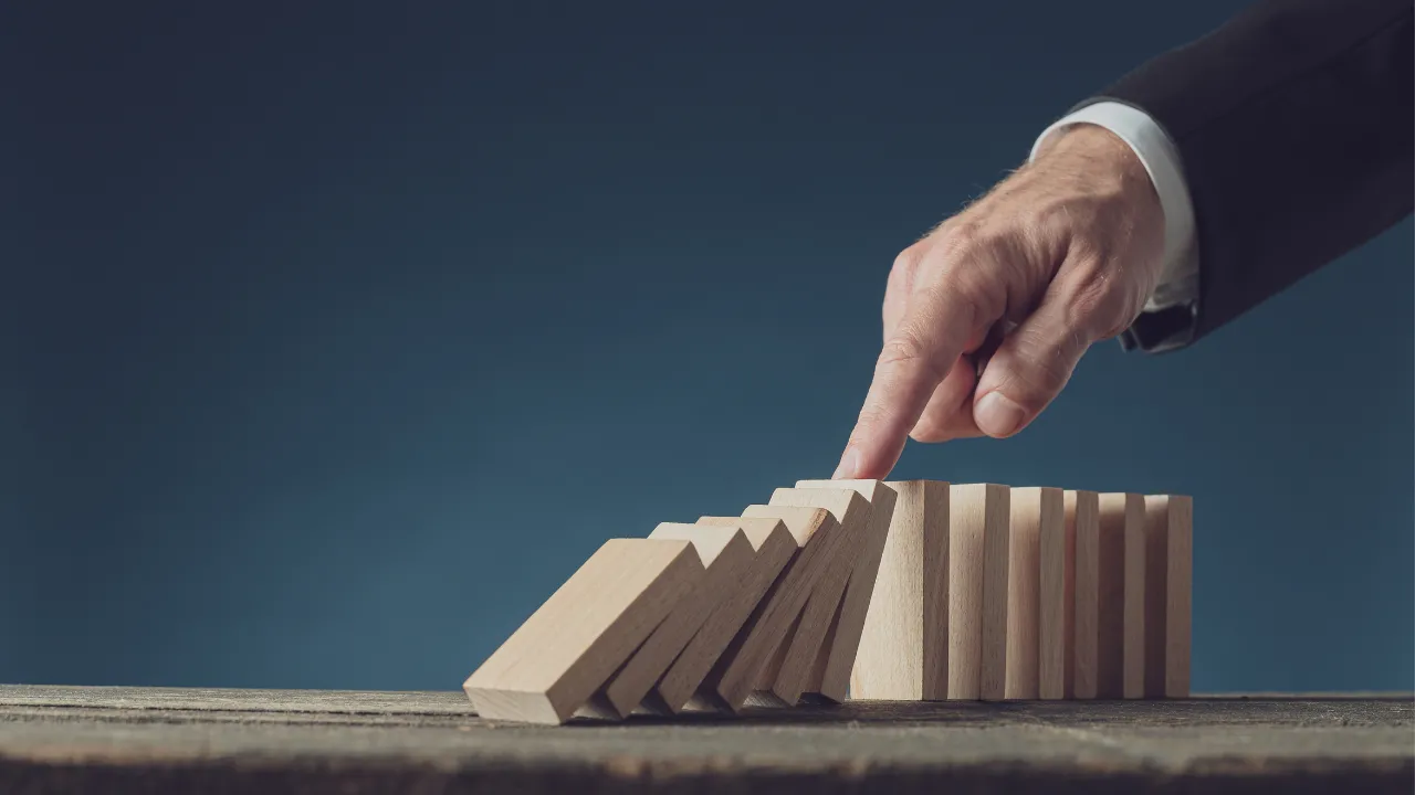 Imagem de uma mão a tentar travar a queda das peças de um dominó