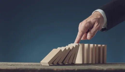 Imagem de uma mão a tentar travar a queda das peças de um dominó