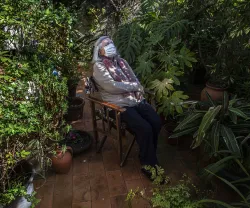 Imagem de uma mulher de máscara num canto do jardim