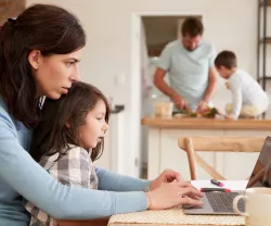 Imagem de uma mulher a trabalhar ao computador com a filha ao colo