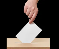 Imagem de uma mão a colocar o voto na urna eleitoral. Crédito: Canva